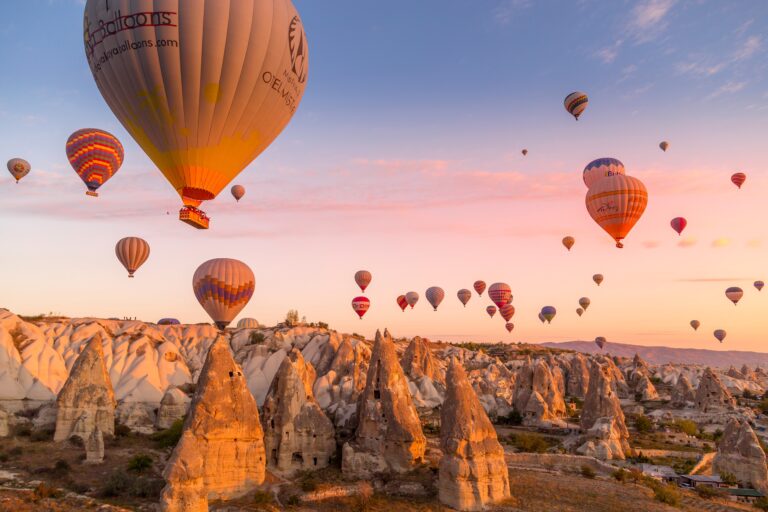 Göreme, Cappadocia, Turkey - October 7 2019:  Hot air balloons filled with tourists during a pink sunrise floating along valleys of Göreme National Park
